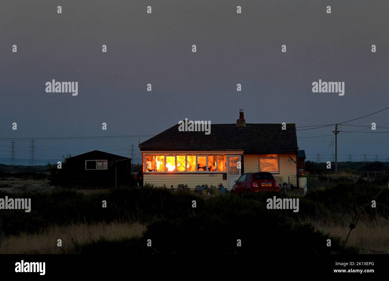 The sun reflects in the windows of a cottage as the sun rises over Dungeness in Kent. Picture date: Wednesday September 21, 2022. Stock Photo