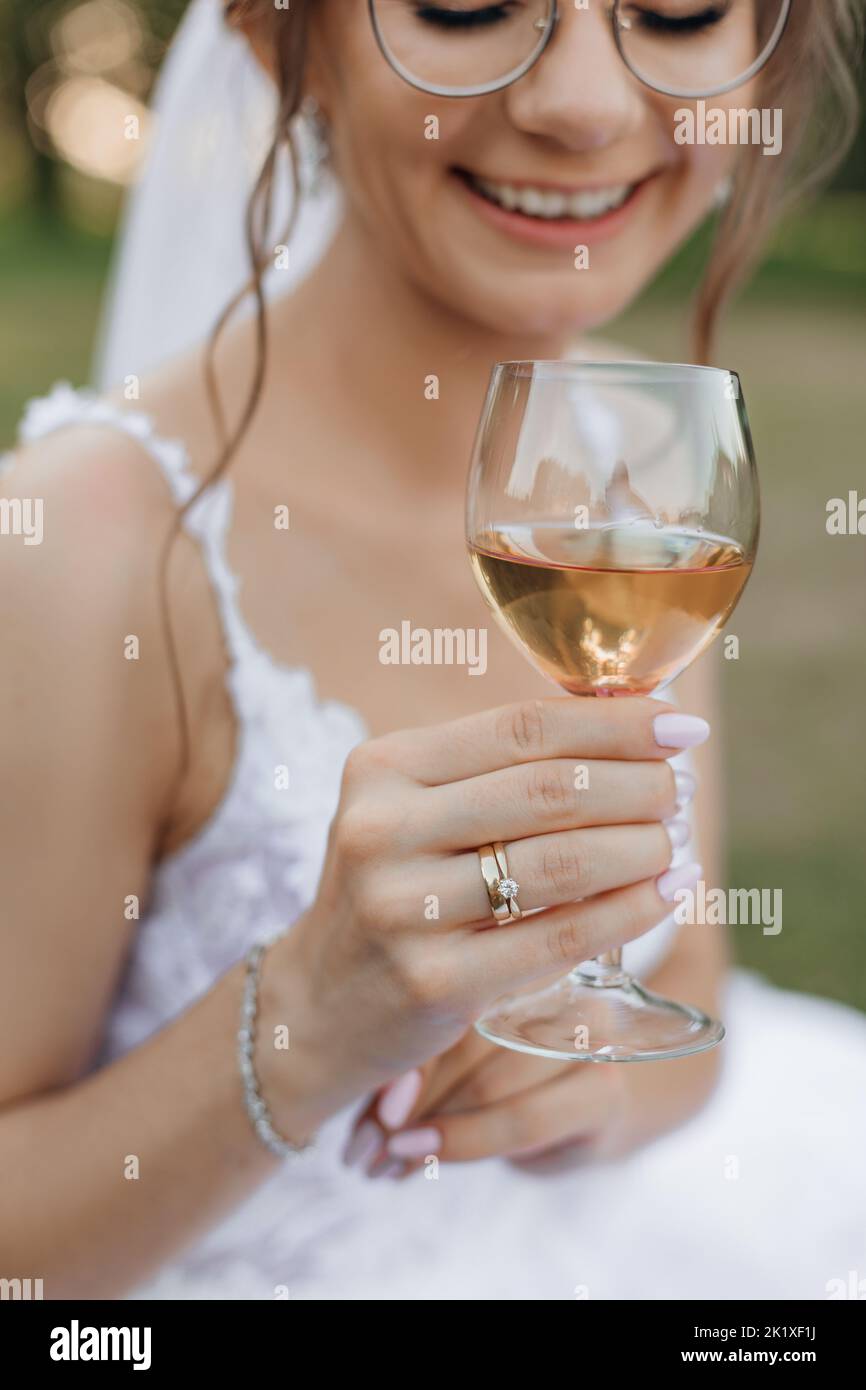 Vertical portrait of cropped smiling bride in wedding dress and veil with glasses drinking bubbly champagne in wineglass Stock Photo