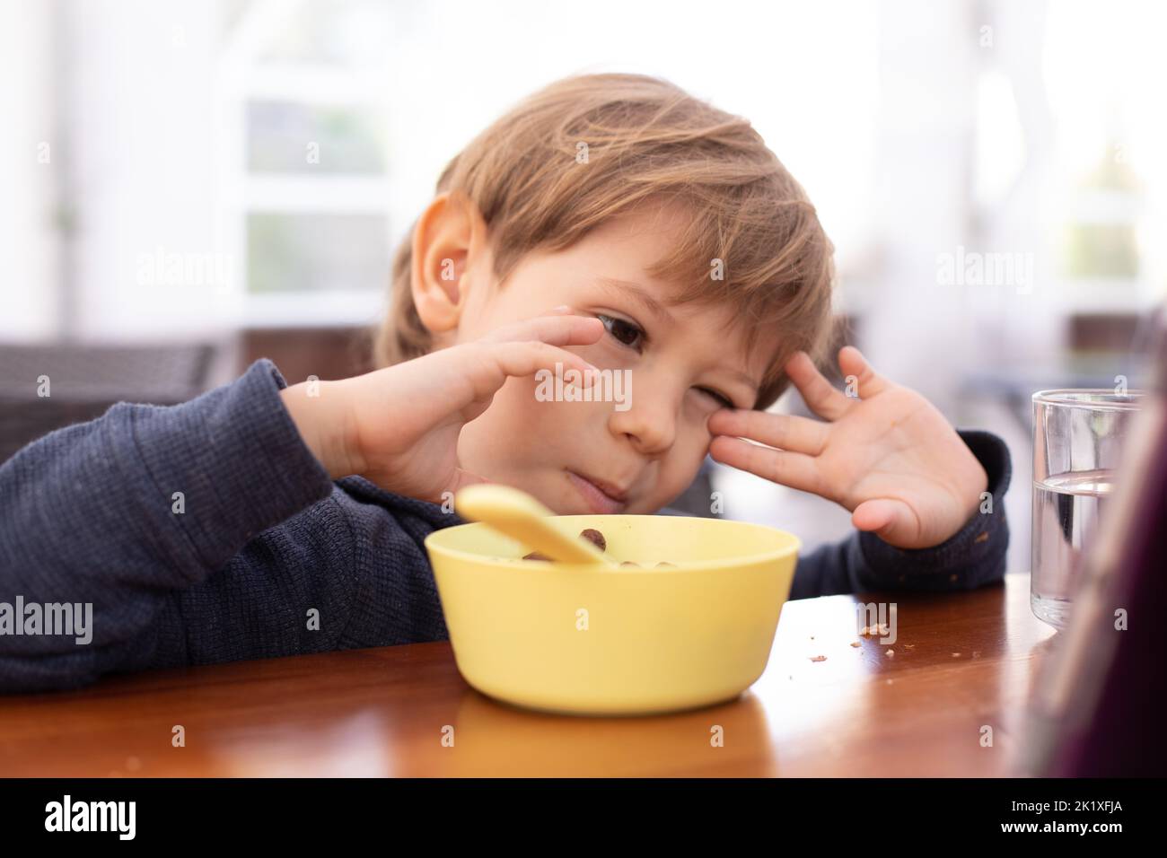 Little boy sit at table and with interest watch cartoon on tablet computer closeup. Kid of kindergarten age eat chocolate balls with milk. Autism Stock Photo