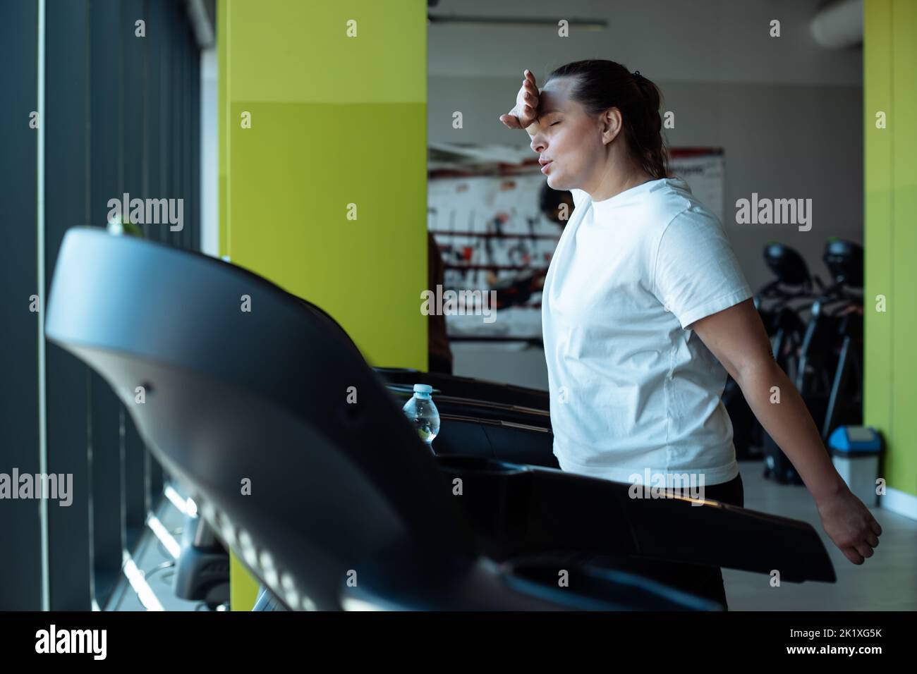 Tired plus size woman run on treadmill at fitness gym wiping sweat from