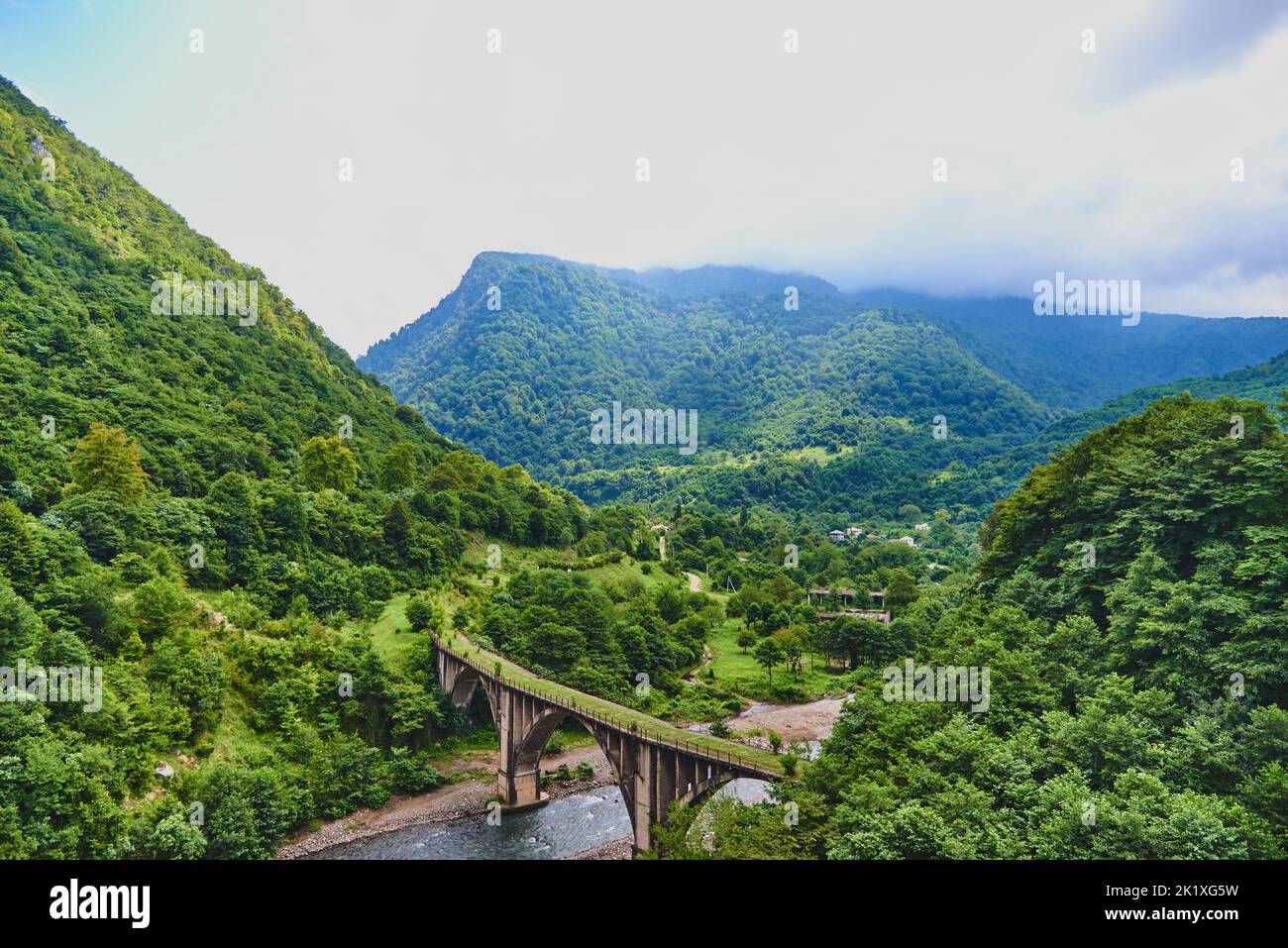 Mountain landscape with an abandoned stone bridge over the river. Thick clouds over the mountains covered with forest. Stock Photo