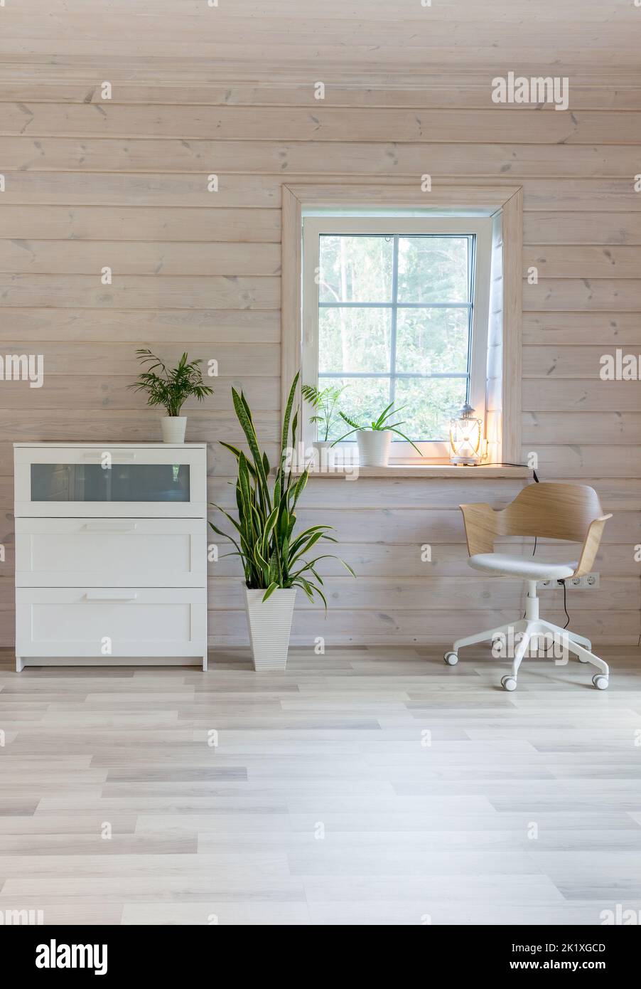 Stylish Scandinavian living room or bedroom with designer furniture, plants, dresser and chair. Wooden light finishing of walls and floor. Stock Photo