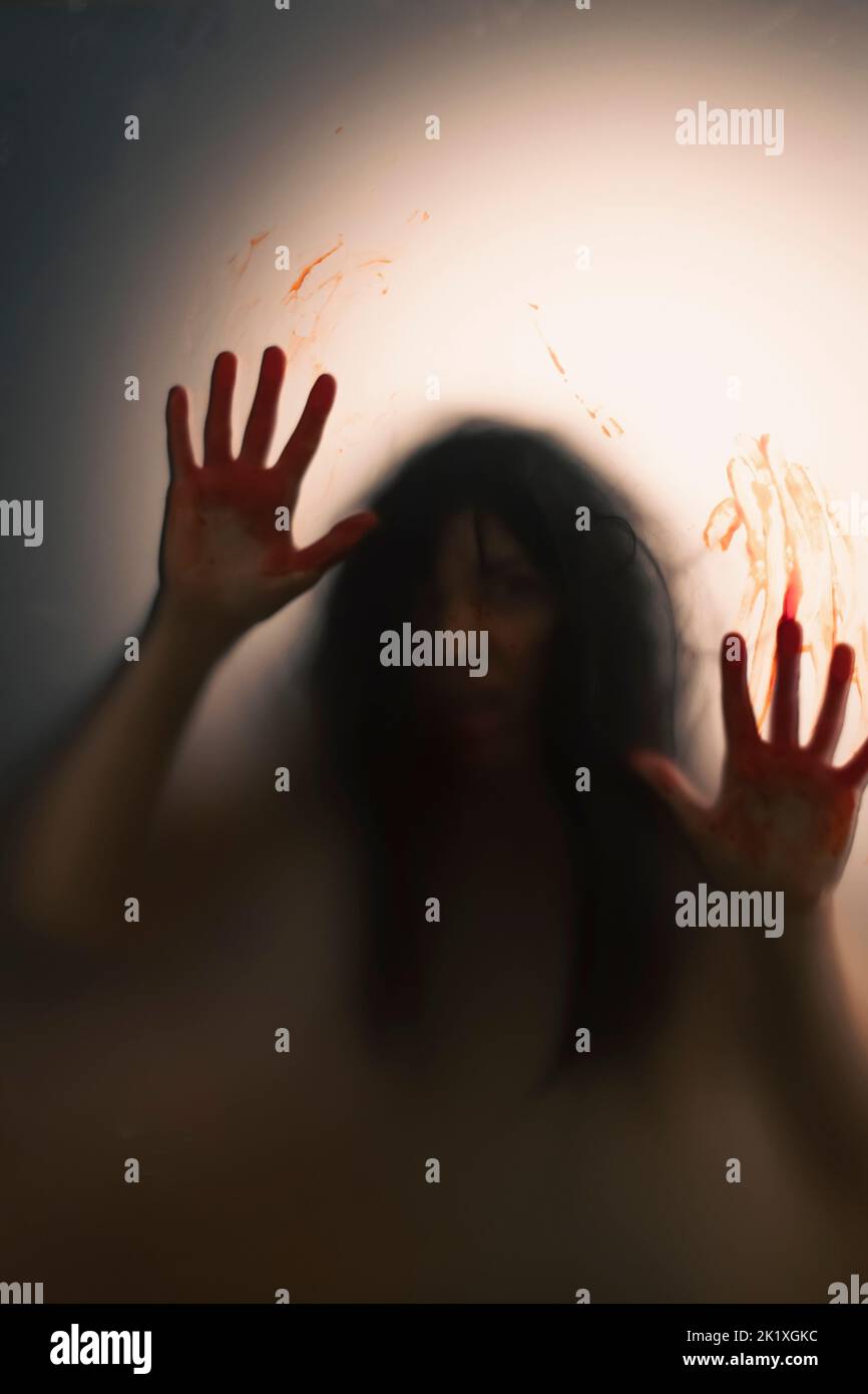 Horror ghost woman with blooded hands behind the matte glass. Halloween festival concept. Stock Photo