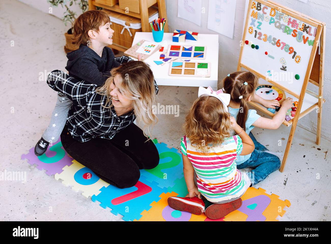 Teacher with children having fun and playing games, learning letters and numbers in kid development childcare center  Stock Photo