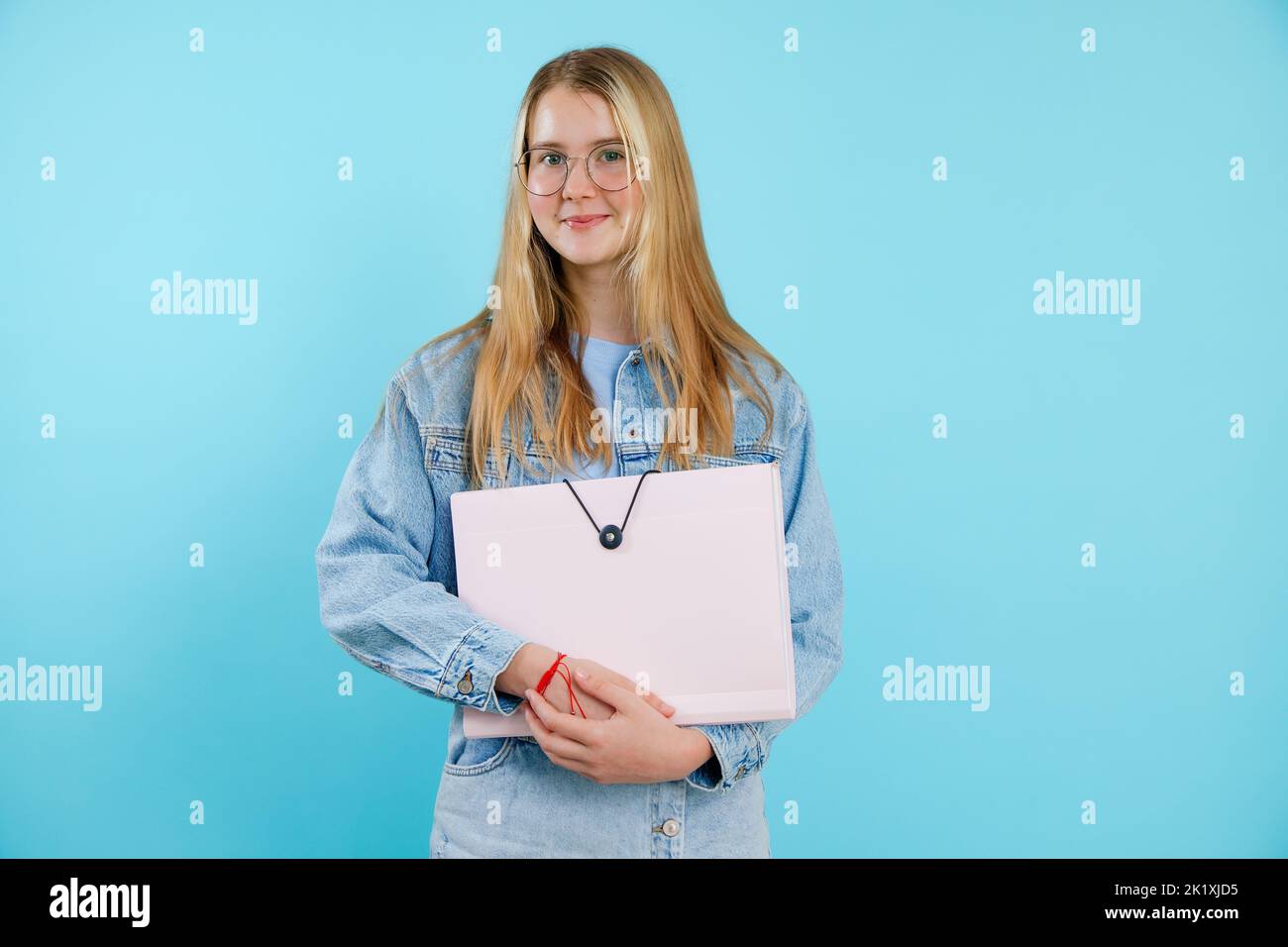 Confident, powerful, smiling blonde teenage girl in glasses holding paper folder, portfolio. Back to school, university Stock Photo