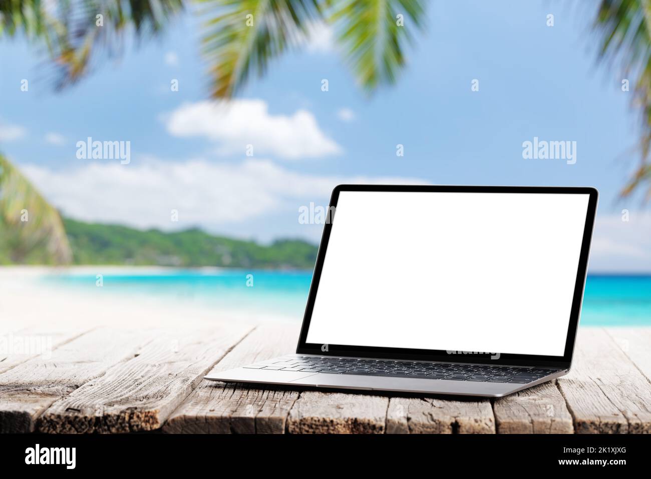 Laptop with blank screen on wooden table in front of sunny sea and palm leaves. Work and travel or remote business concept Stock Photo