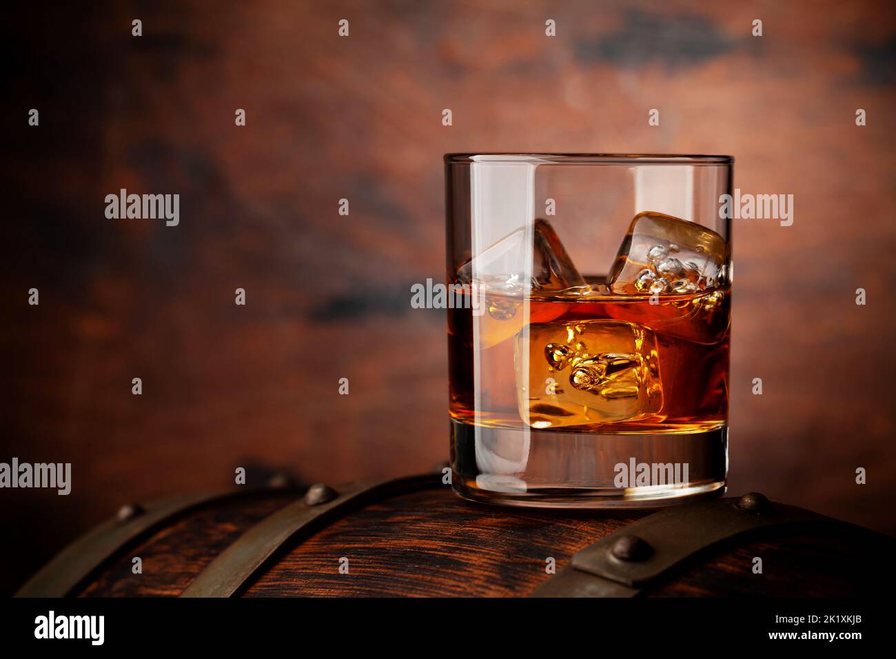 Glass of whiskey with ice cubes on the old barrel. With copy space on wooden background Stock Photo