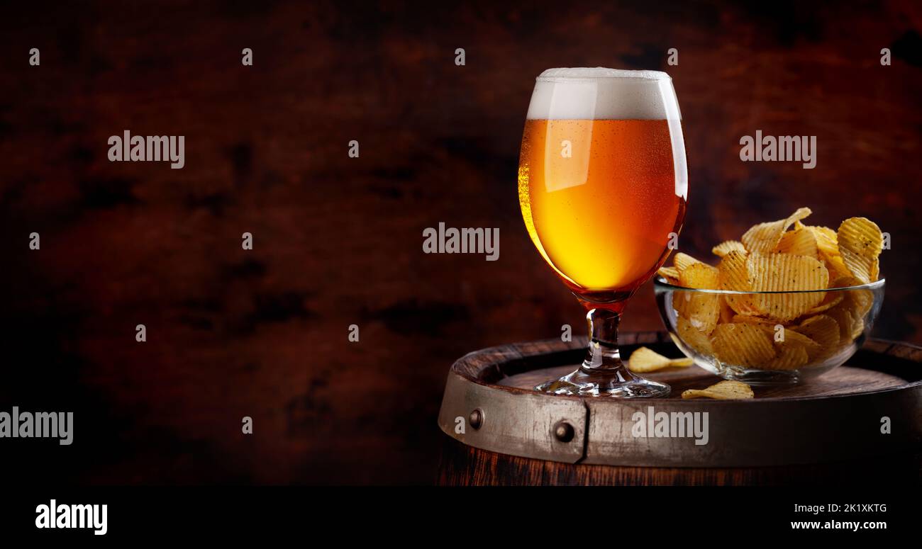 Beer glass and potato chips on wooden barrel. With copy space Stock Photo