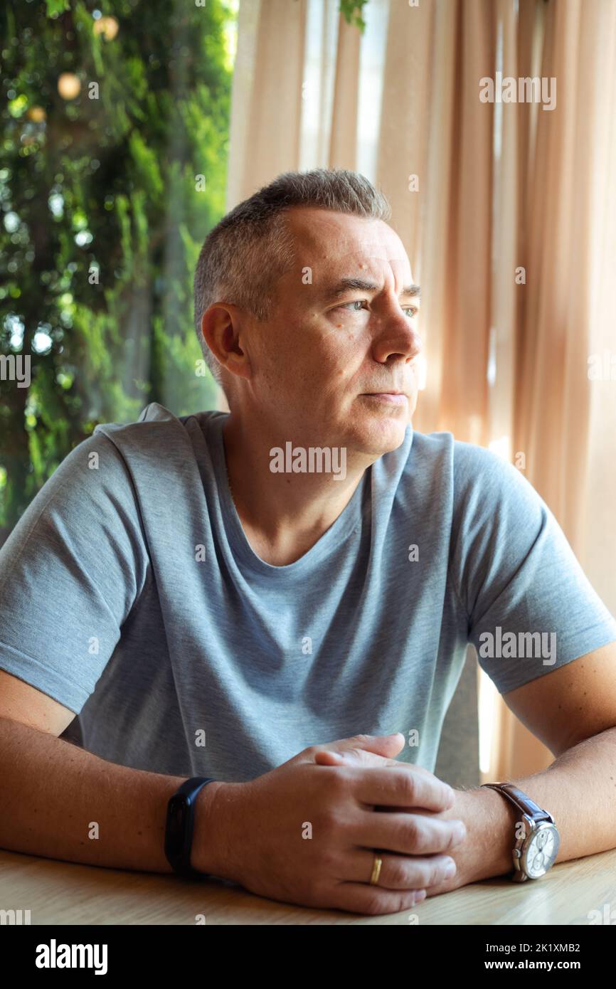 Mature thoughtful business man sitting at table in cafe and looking at window. Handsome gray haired 50 years old man resting in cafe. Modern lifestyle Stock Photo