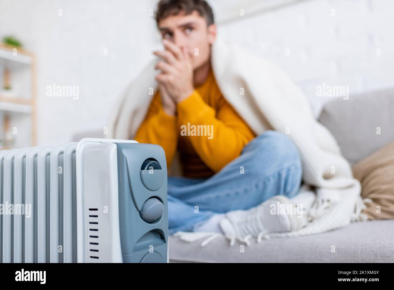modern radiator heater near blurred man covered in blanket sitting on