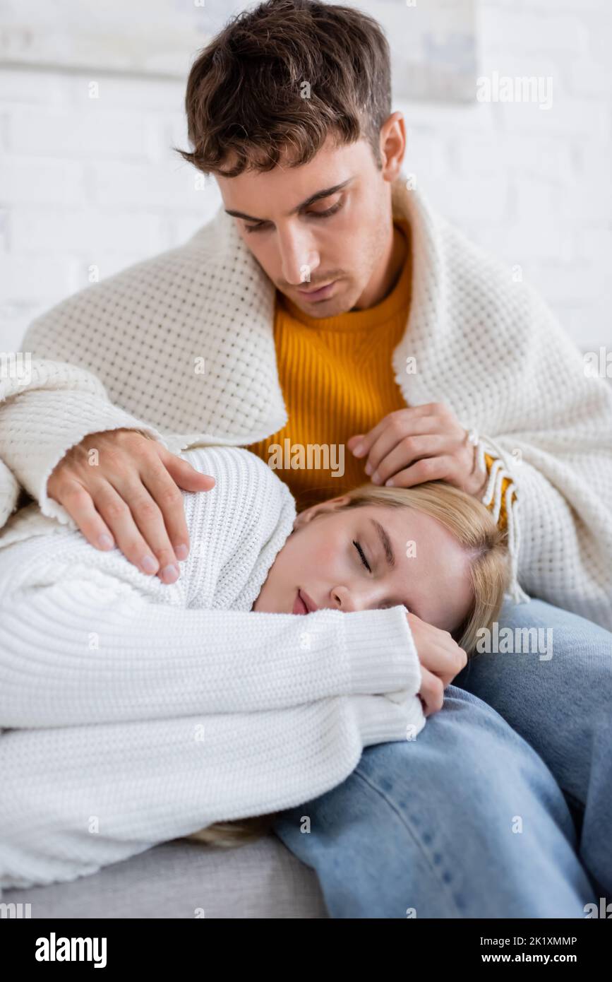 young woman covered in blanket sleeping on legs of caring boyfriend in