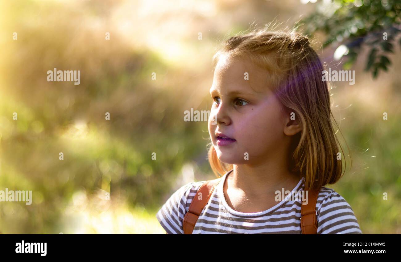 Smiling little girl in the park. Copy space. Happy child looking away. Portrait of a laughing kid outside. Banner. Stock Photo