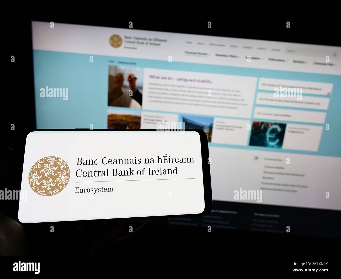 Person holding mobile phone with logo of financial institution Central Bank of Ireland on screen in front of web page. Focus on phone display. Stock Photo