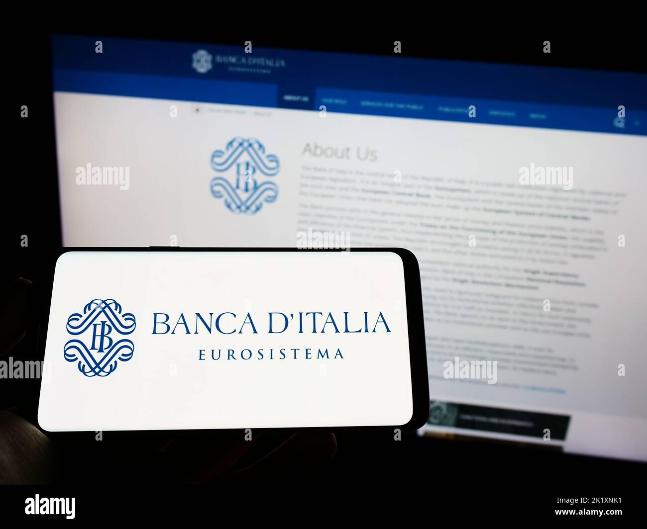 Person holding mobile phone with logo of Italian central bank Banca d'Italia on screen in front of web page. Focus on phone display. Stock Photo