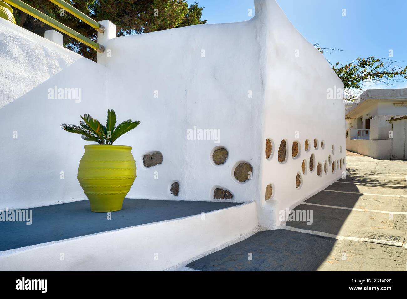 Stylish Mediterranean alleyway or street, classic whitewashed walls, stone pavement, decorative golden vase with palm seedling. Minimalistic design Stock Photo