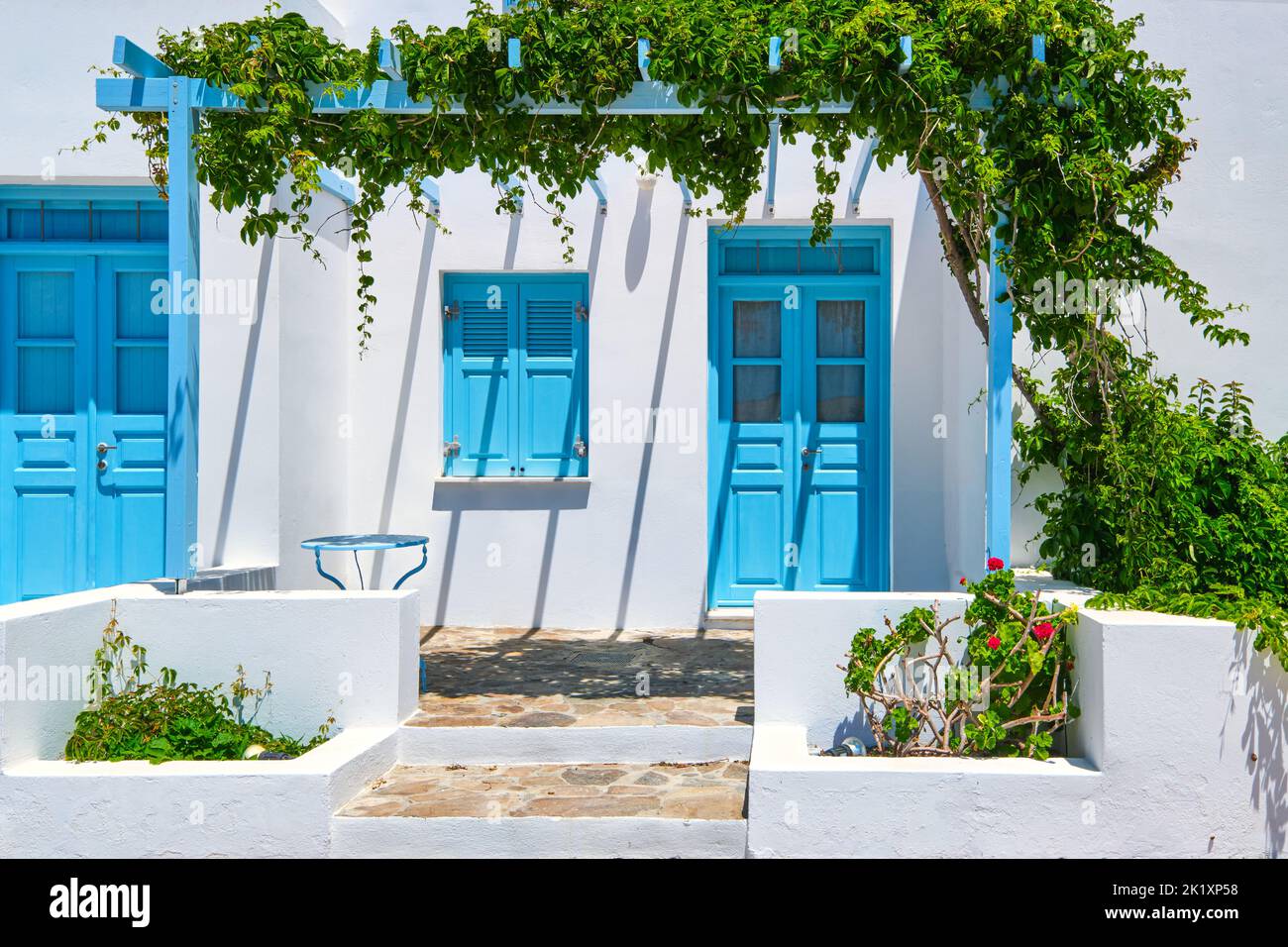 Traditional blue doors and windows, whitewashed walls of Greek houses. Midday summer sunshine, blue table, pavement, vine, porch, Milos, Greece Stock Photo