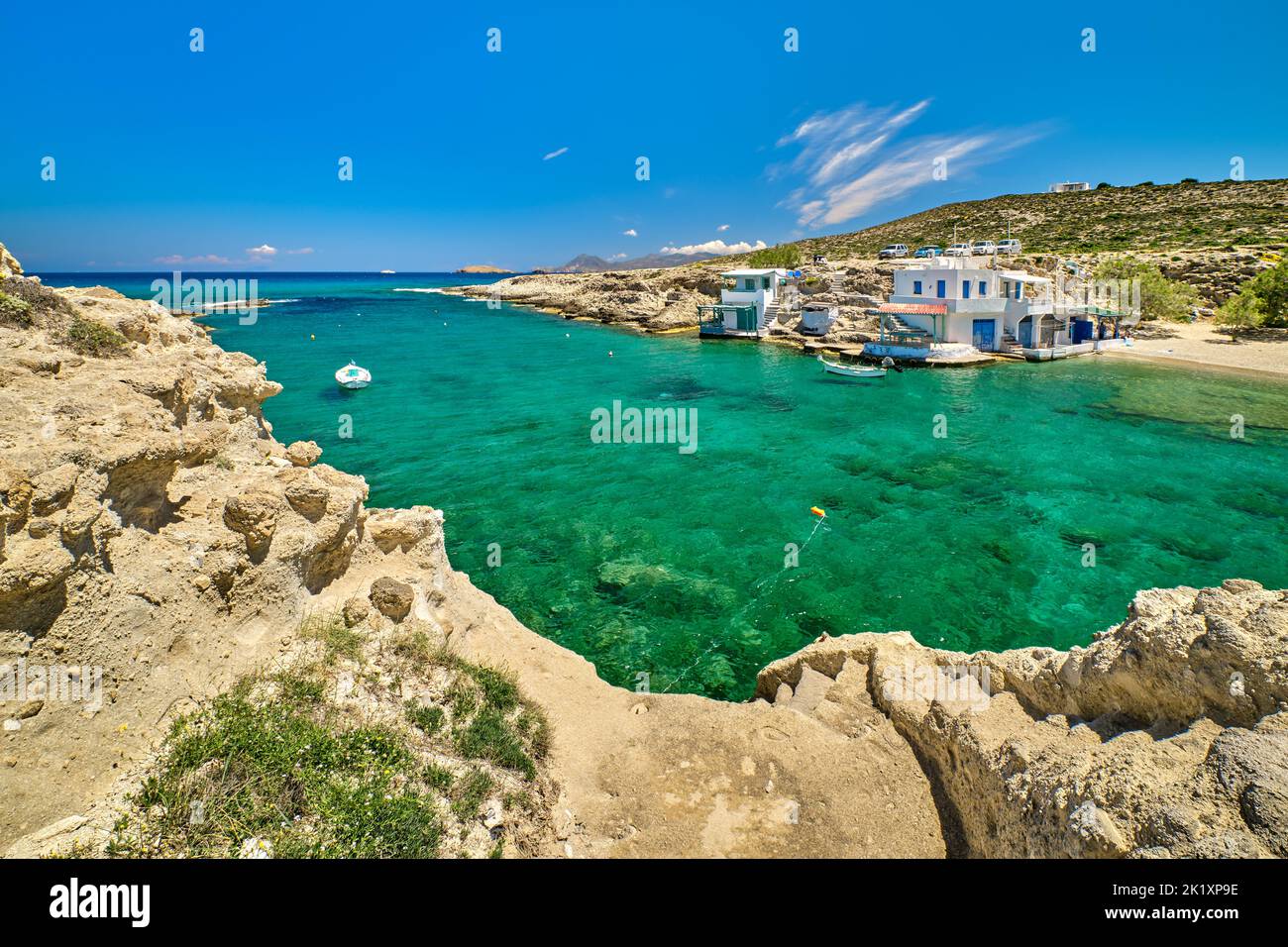 Beautiful view of secluded Mediterranean island bay on summer day. Whitewashed houses, hills, clear sky, azure sea waters, beach. Milos, Greece Stock Photo