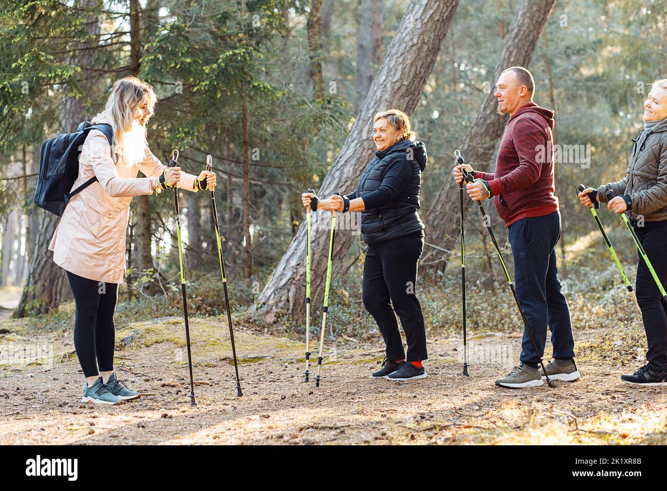 Smiling woman coach with group of people teach Scandinavian, Nordic walking exercises. Education for joying campers. Stock Photo