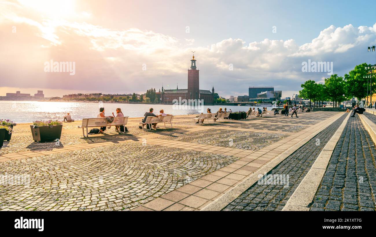 STOCKHOLM, SWEDEN - JUNE 11, 2022: People relaxing on sunny summer day at Evert Taubes Terrace. Embankment with Stockholms Stadshus on background. Stock Photo