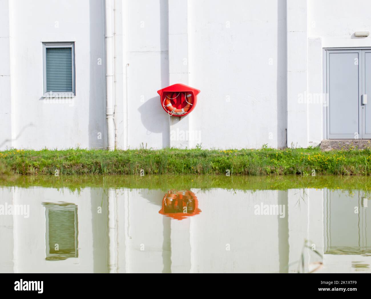 Essex, Britain, 2022. Building exterior and bright red buoy reflected in lake water. Stock Photo