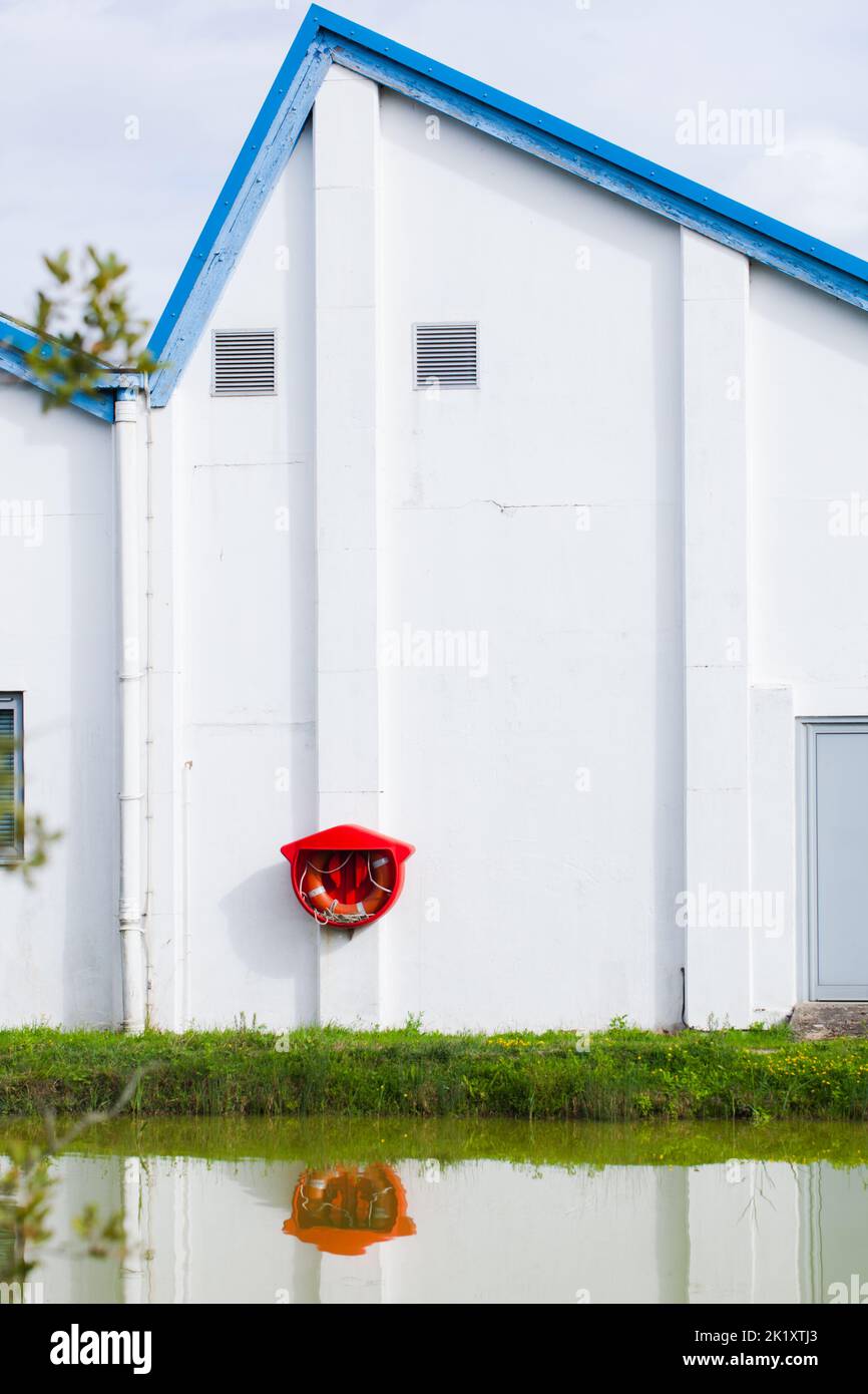 Essex, Britain, 2022. Building exterior and bright red buoy reflected in lake water. Stock Photo