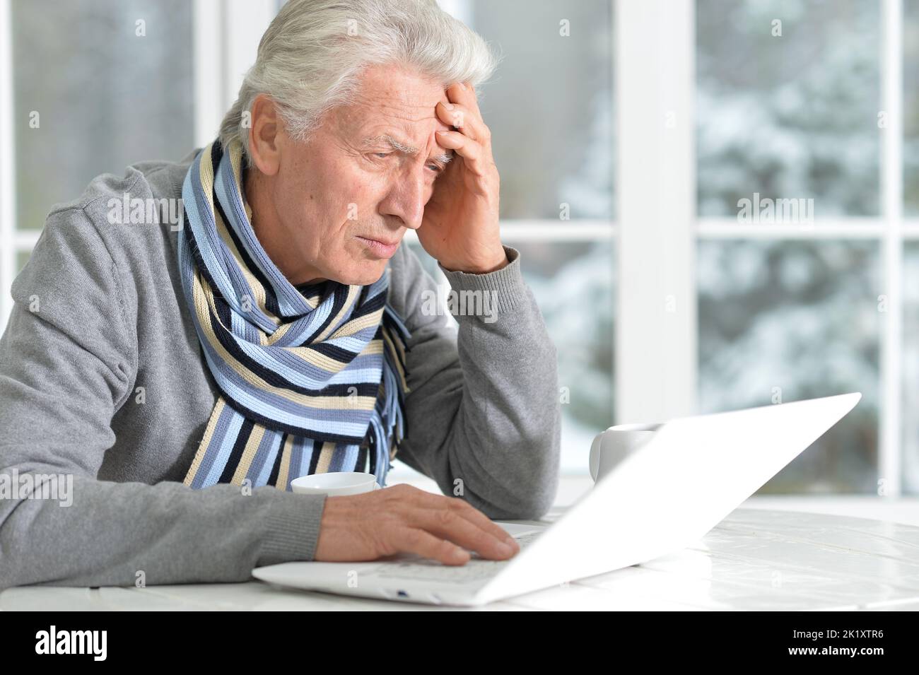 Elderly man sits on the background of the window in winter Stock Photo