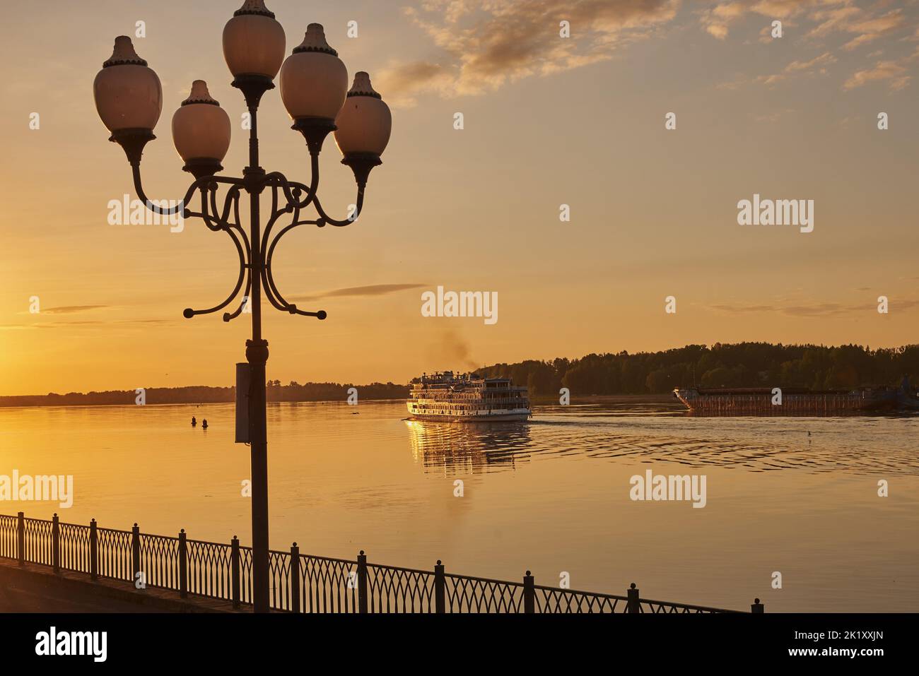 A large tourist ship sailing along the Volga, illuminated by the rays of the setting sun. Stock Photo