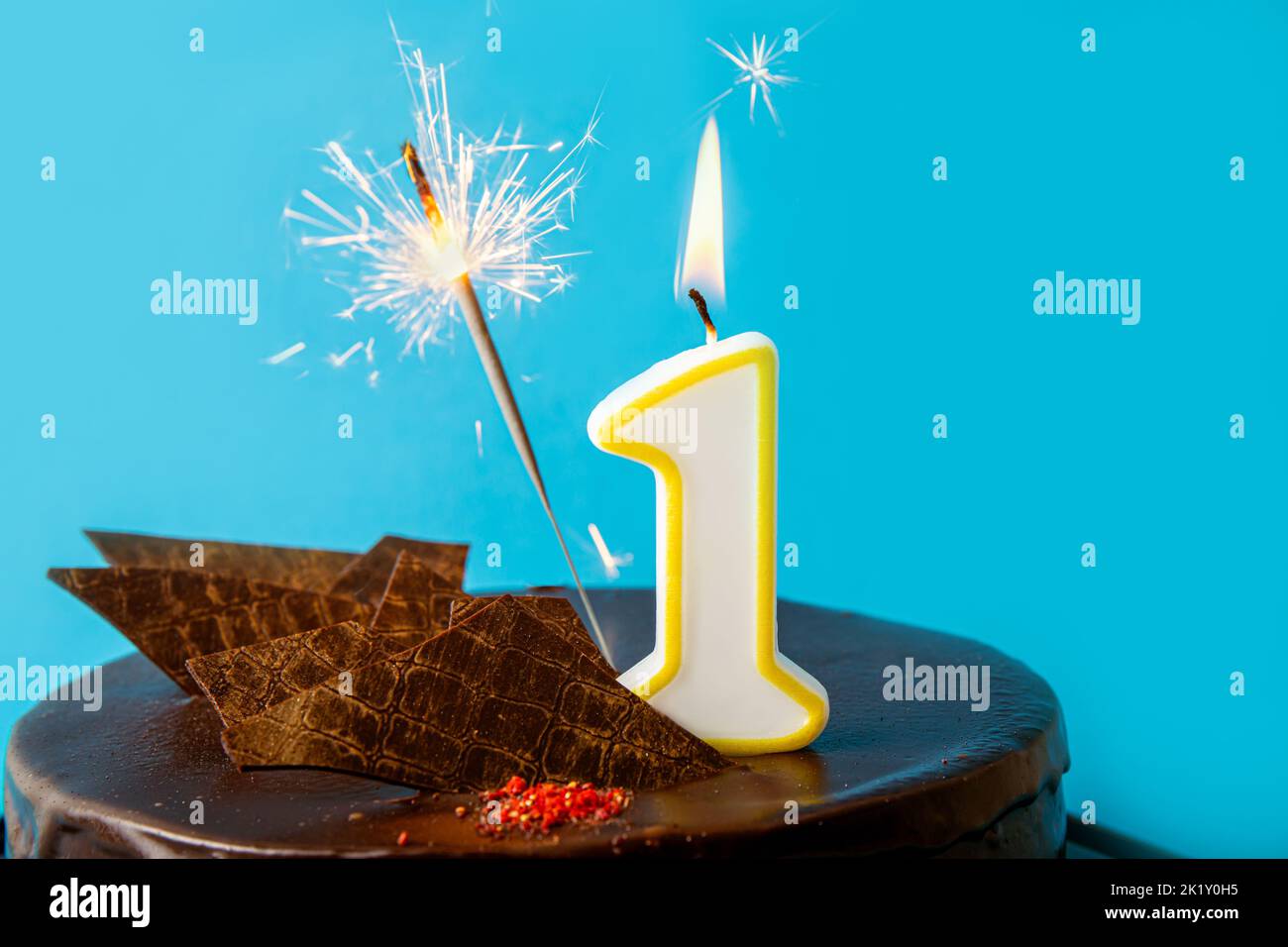 Number 1 birthday candle burning and sparkler with sparks fly on cake. The first birthday of anniversary celebration concept. Lot of copy space. Stock Photo