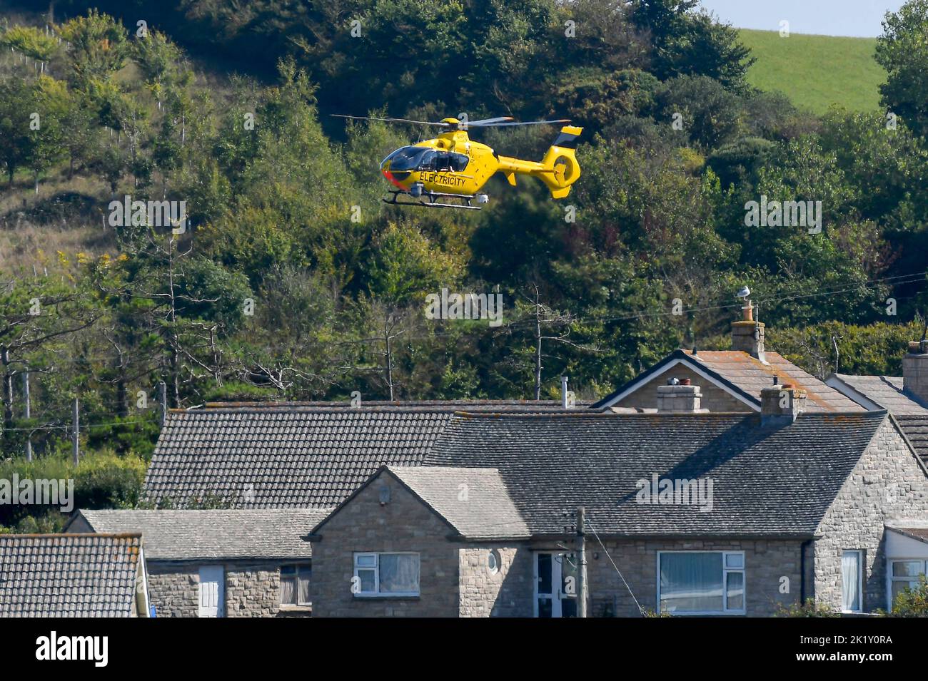 Burton Bradstock, Dorset, UK, 21st September 2022.  A yellow electricity helicopter flying low over electricity power lines checking for faults near houses at Burton Bradstock in Dorset.  Picture Credit: Graham Hunt/Alamy Live News Stock Photo