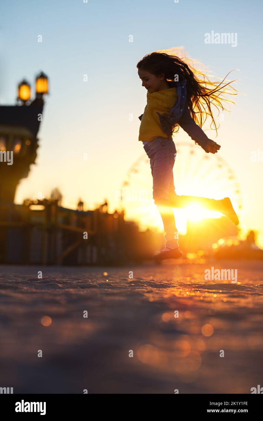 Happy girl jumping on the beach sand and enjoying the sunset in the fun city Stock Photo