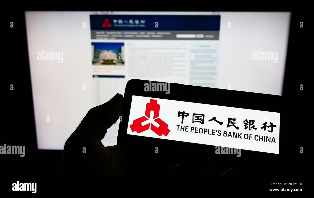 Person holding smartphone with logo of financial institution People's Bank of China on screen in front of website. Focus on phone display. Stock Photo