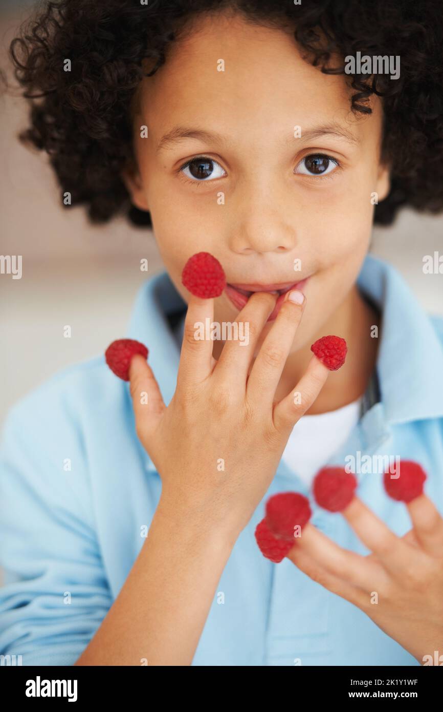 I love raspberries. Portrait of a cute young boy with raspberries on his fingers. Stock Photo