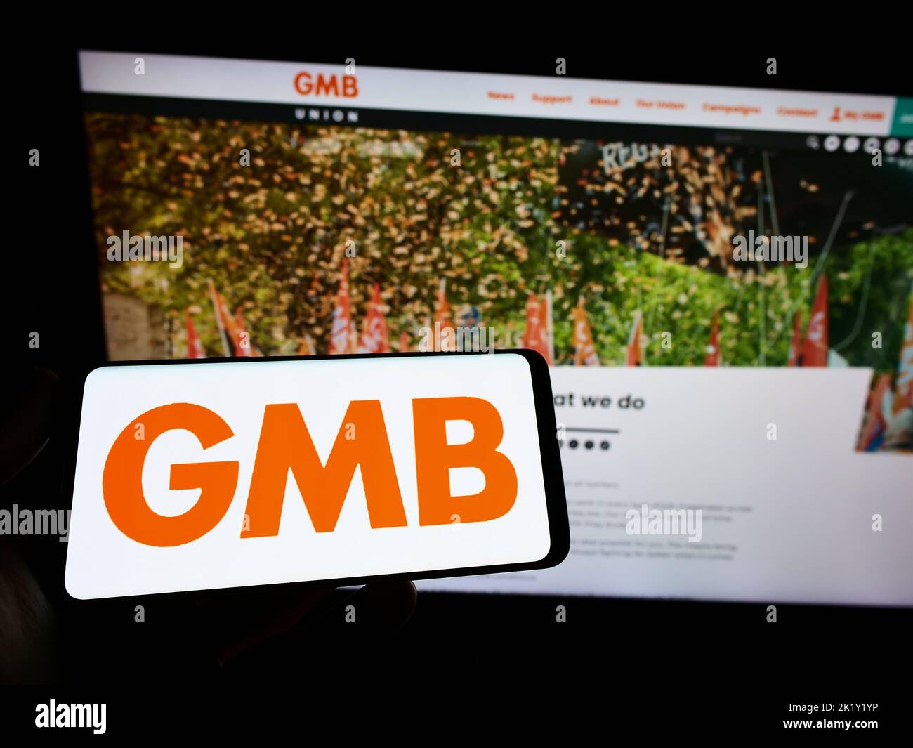 Person holding smartphone with logo of British trade union GMB on screen in front of website. Focus on phone display. Stock Photo