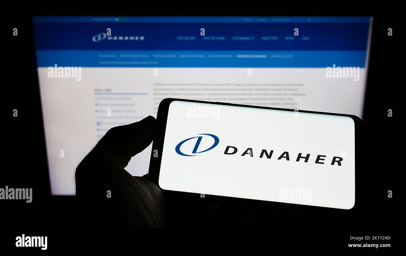 Person holding mobile phone with logo of American conglomerate Danaher Corporation on screen in front of web page. Focus on phone display. Stock Photo