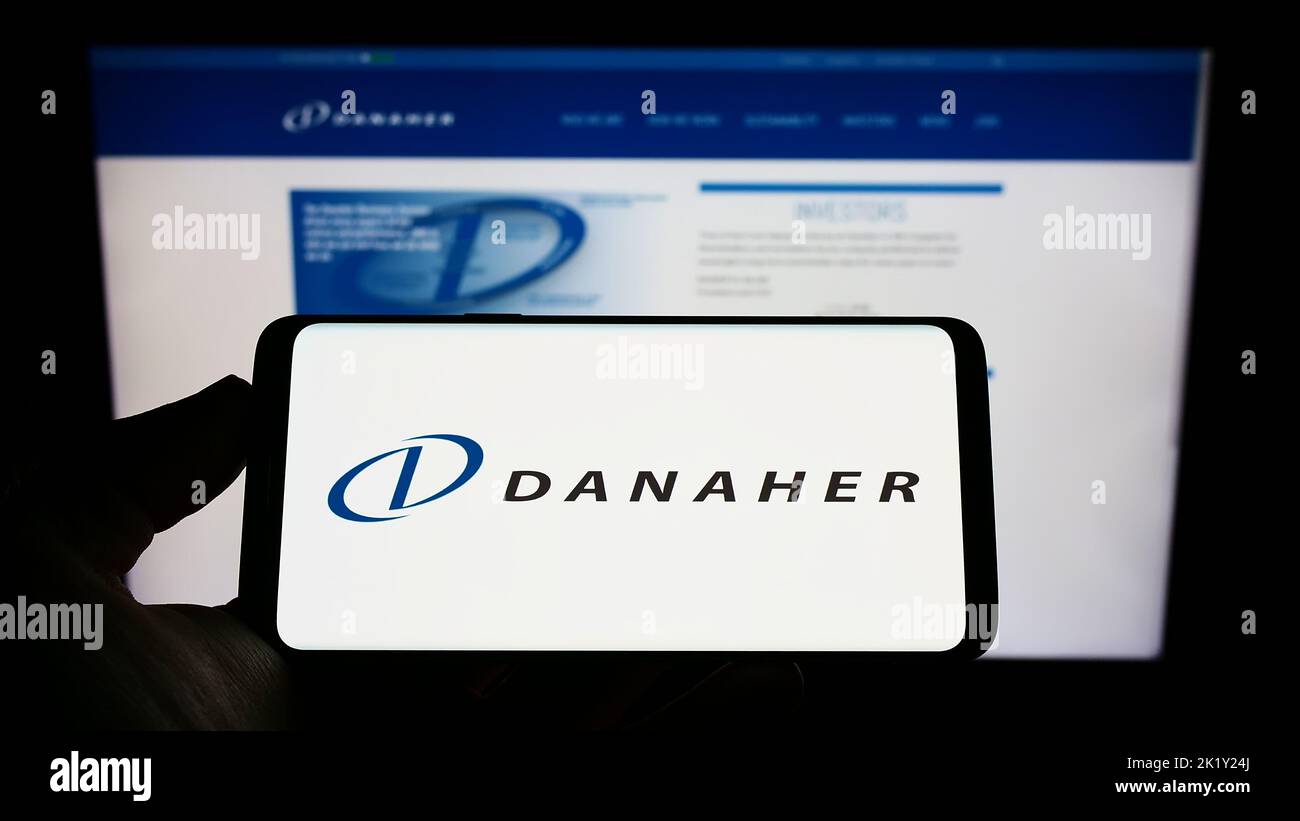 Person holding smartphone with logo of US conglomerate Danaher Corporation on screen in front of website. Focus on phone display. Stock Photo