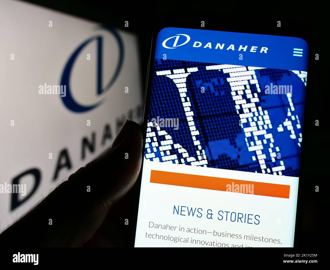Person holding smartphone with website of US conglomerate Danaher Corporation on screen in front of logo. Focus on center of phone display. Stock Photo