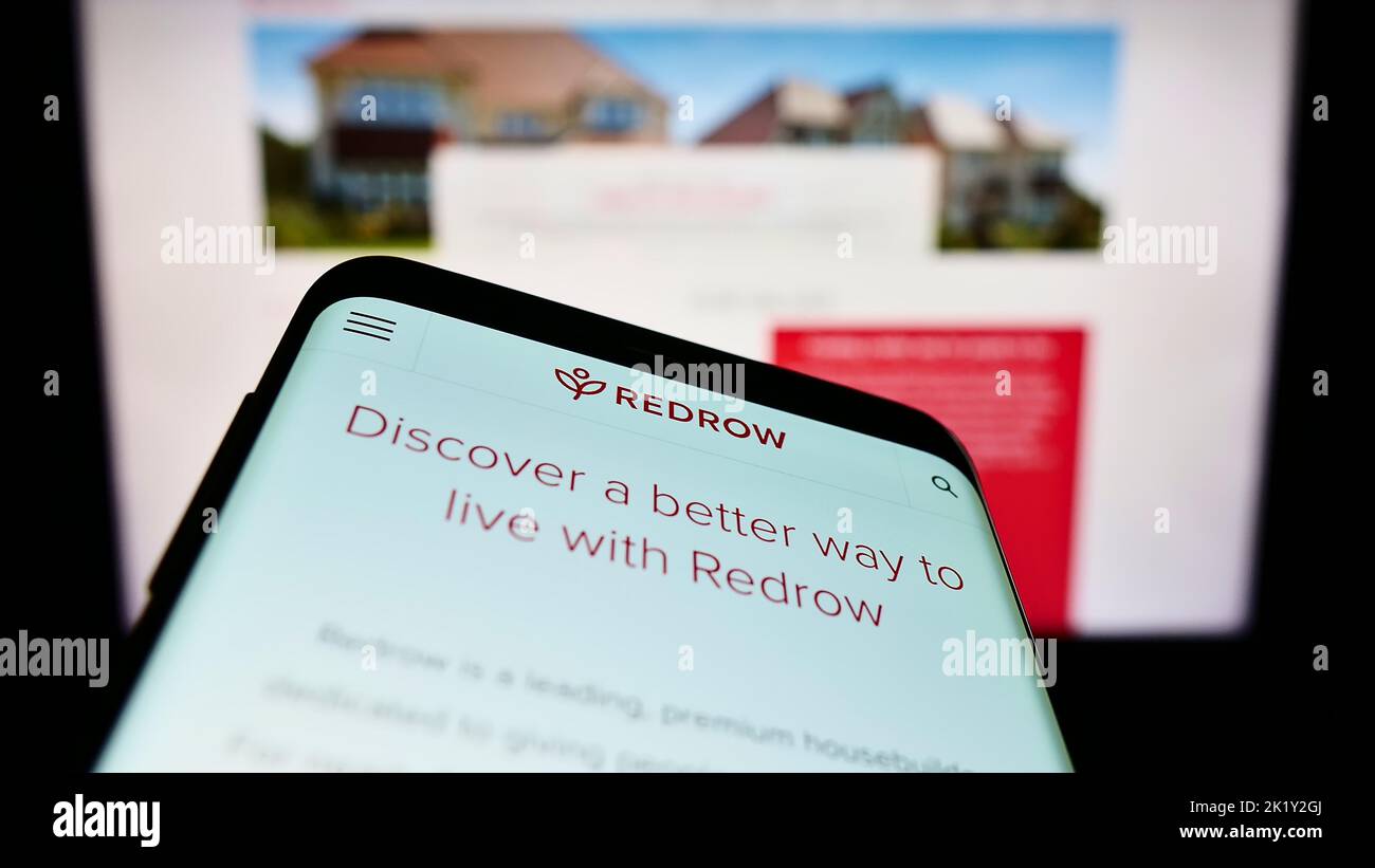 Mobile phone with website of British housebuilding company Redrow plc on screen in front of business logo. Focus on top-left of phone display. Stock Photo