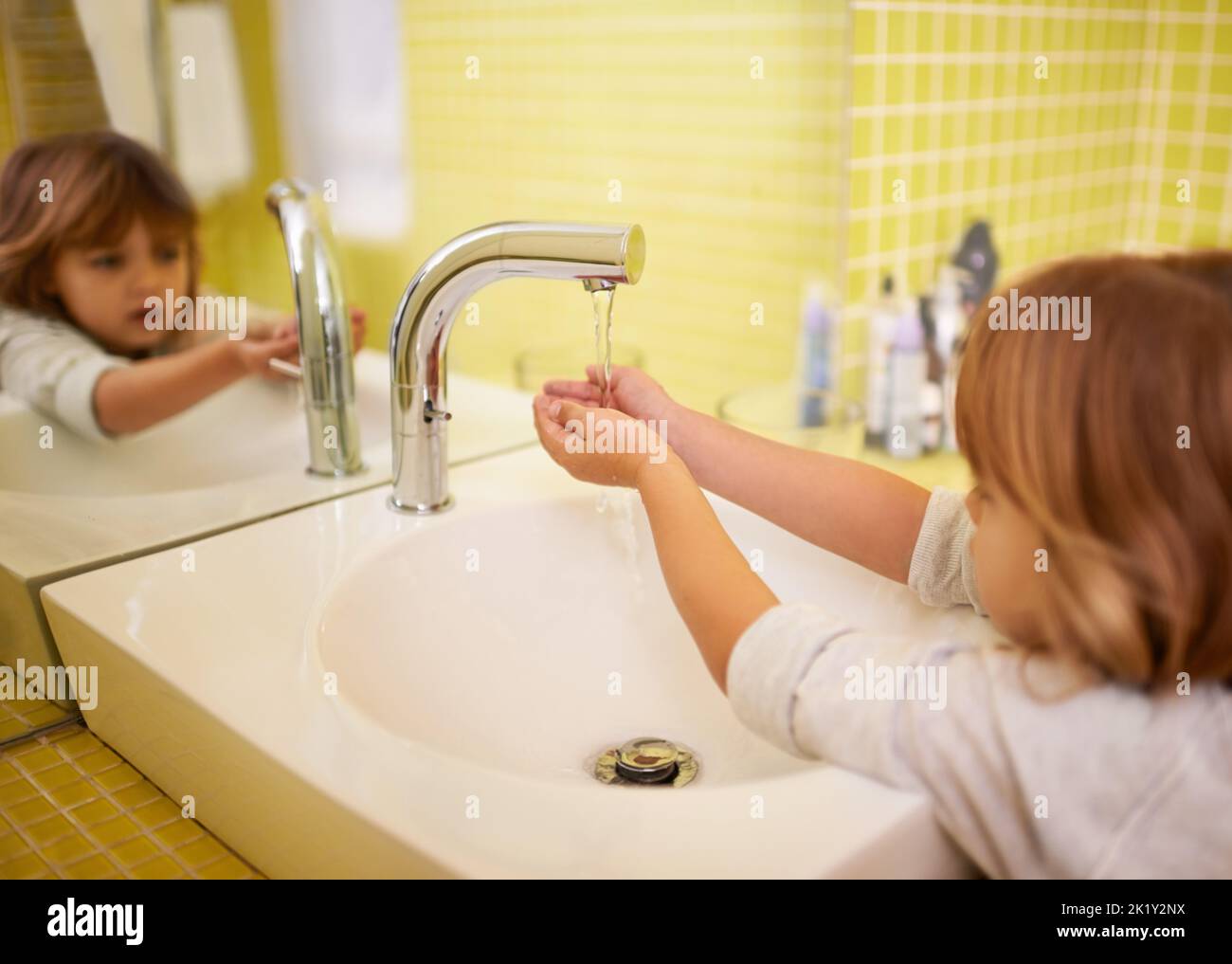 Because Mom said I have to. A cute little girl washing her hands in the bathroom basin. Stock Photo