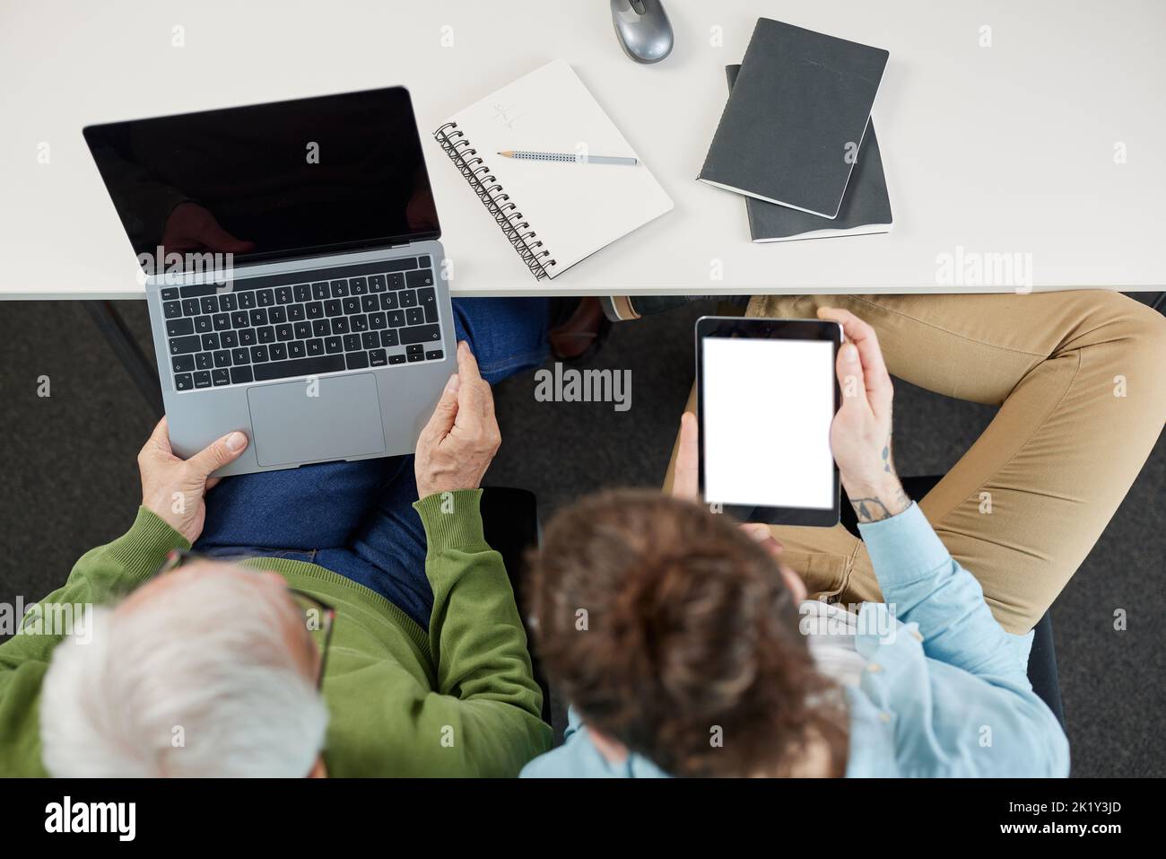 Top view of a teacher holds tablet and shows senior student how to do web design on a laptop. Stock Photo