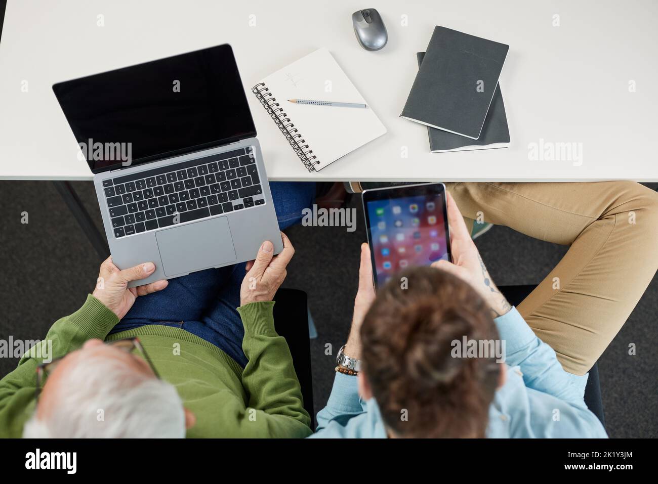 Top view of a senior man and his young teacher using technologies in educational purposes. Stock Photo