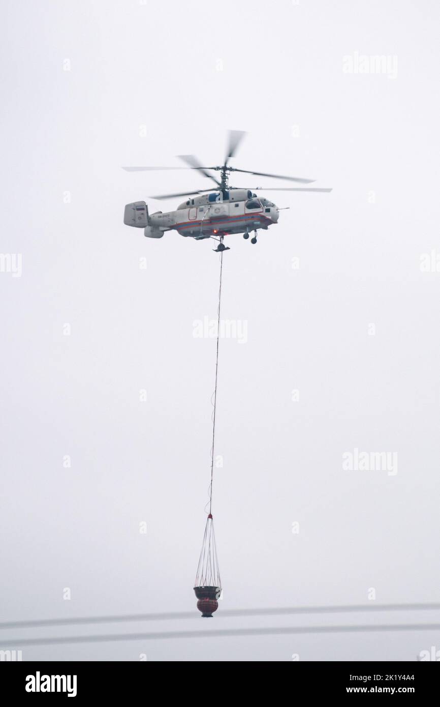 A fire helicopter carries a container of water to extinguish a fire in a production building Stock Photo