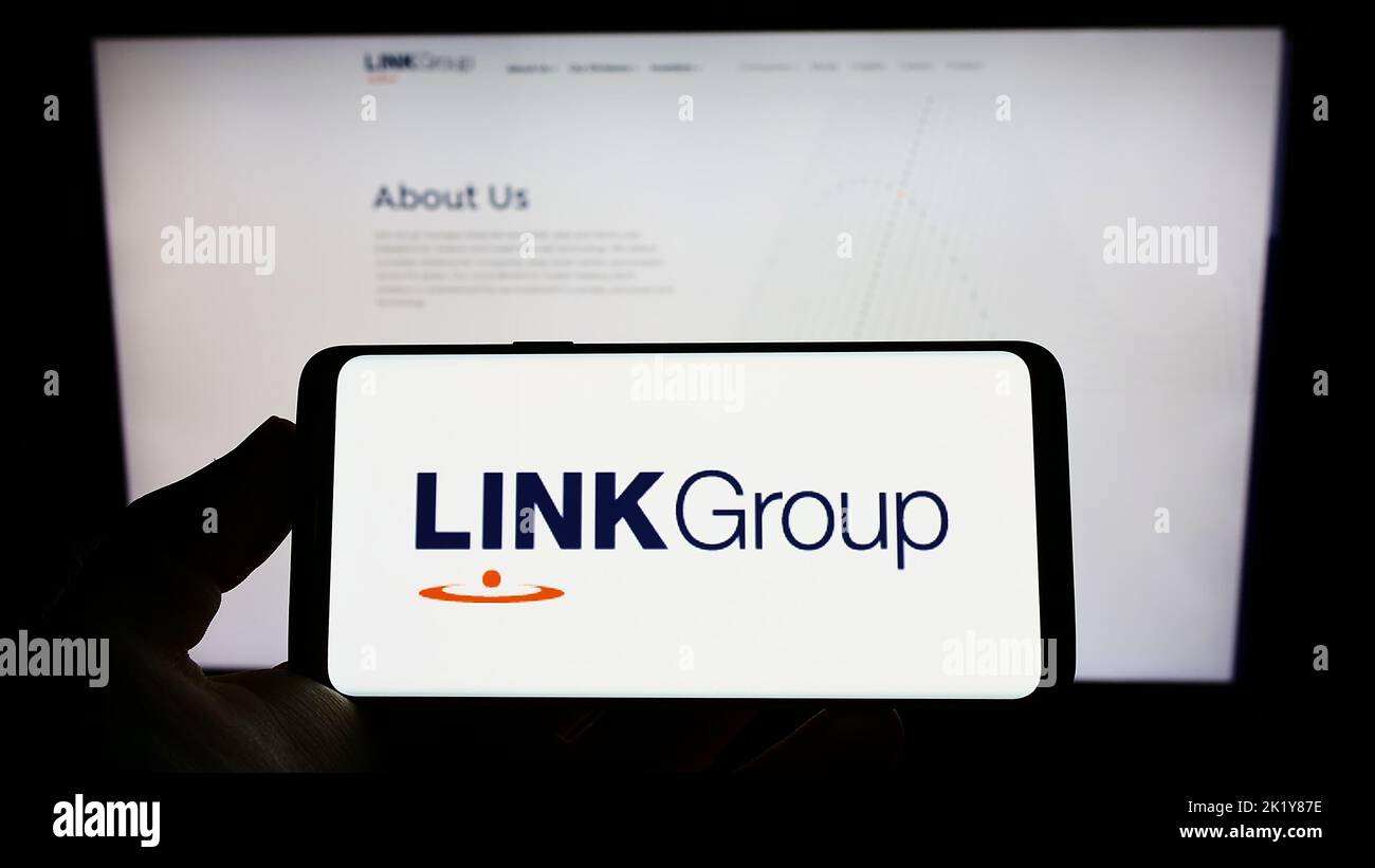 Person holding mobile phone with logo of Australian financial company Link Group on screen in front of business web page. Focus on phone display. Stock Photo