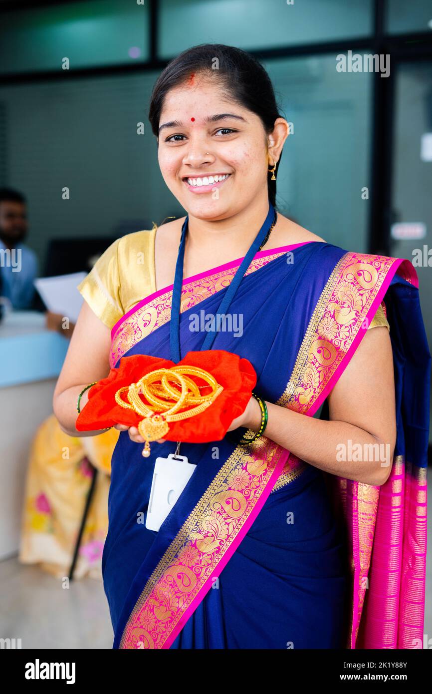 vertical shot of happy smiling woman at bank with gold jewelry in hand looking camera at bank - concept of gold loan, financial or banking service and Stock Photo