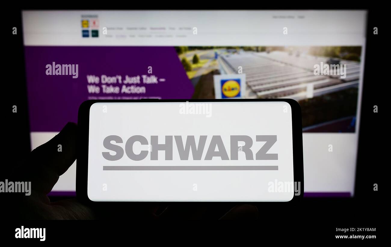 Person holding mobile phone with logo of German retail company Schwarz Group on screen in front of business web page. Focus on phone display. Stock Photo