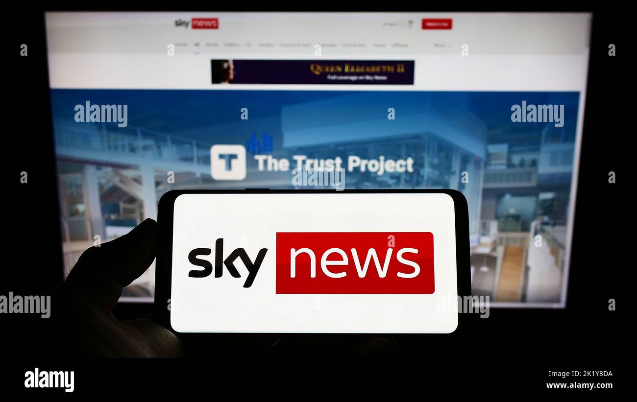 Person holding smartphone with logo of British television channel Sky News on screen in front of website. Focus on phone display. Stock Photo