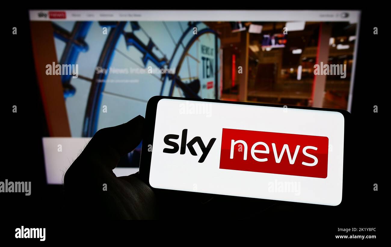 Person holding mobile phone with logo of British television channel Sky News on screen in front of business web page. Focus on phone display. Stock Photo