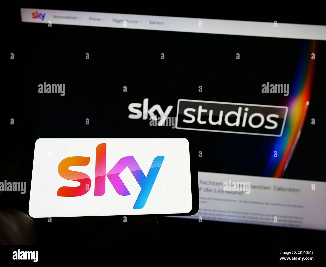 Person holding cellphone with logo of British media company Sky Group Limited on screen in front of business webpage. Focus on phone display. Stock Photo