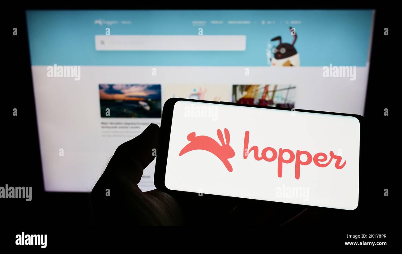 Person holding smartphone with logo of Canadian travel company Hopper Inc. on screen in front of website. Focus on phone display. Stock Photo