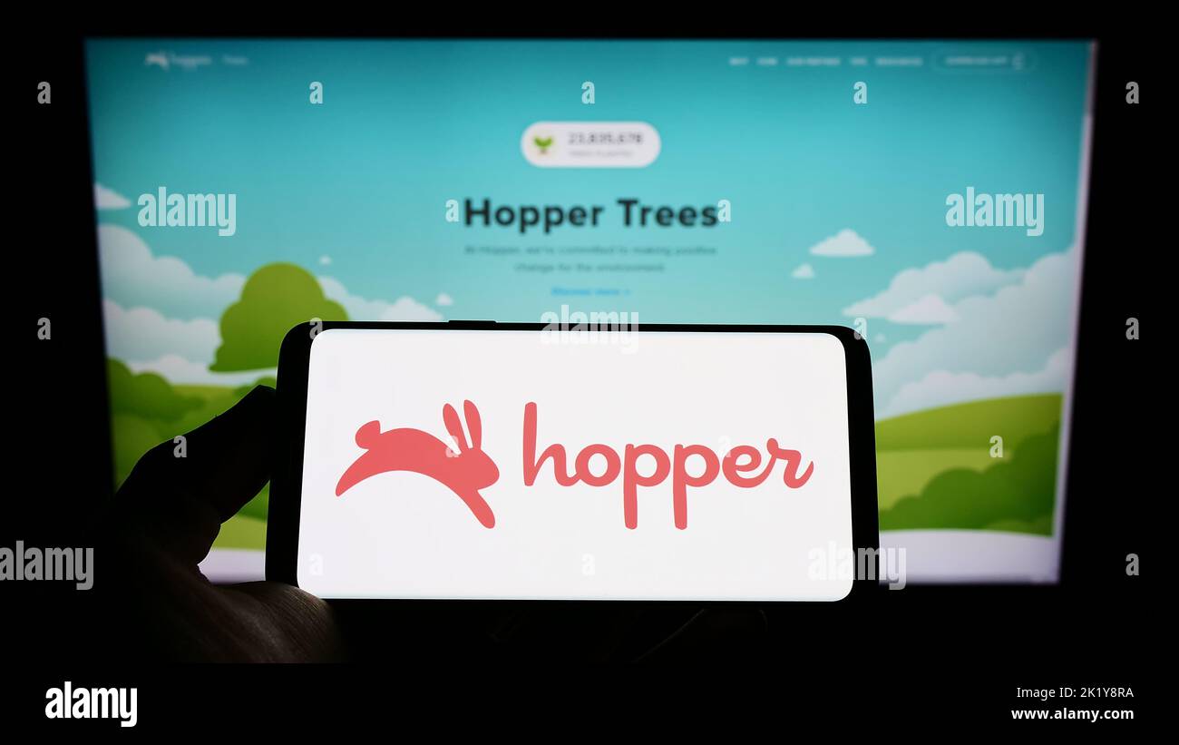 Person holding cellphone with logo of Canadian travel company Hopper Inc. on screen in front of business webpage. Focus on phone display. Stock Photo