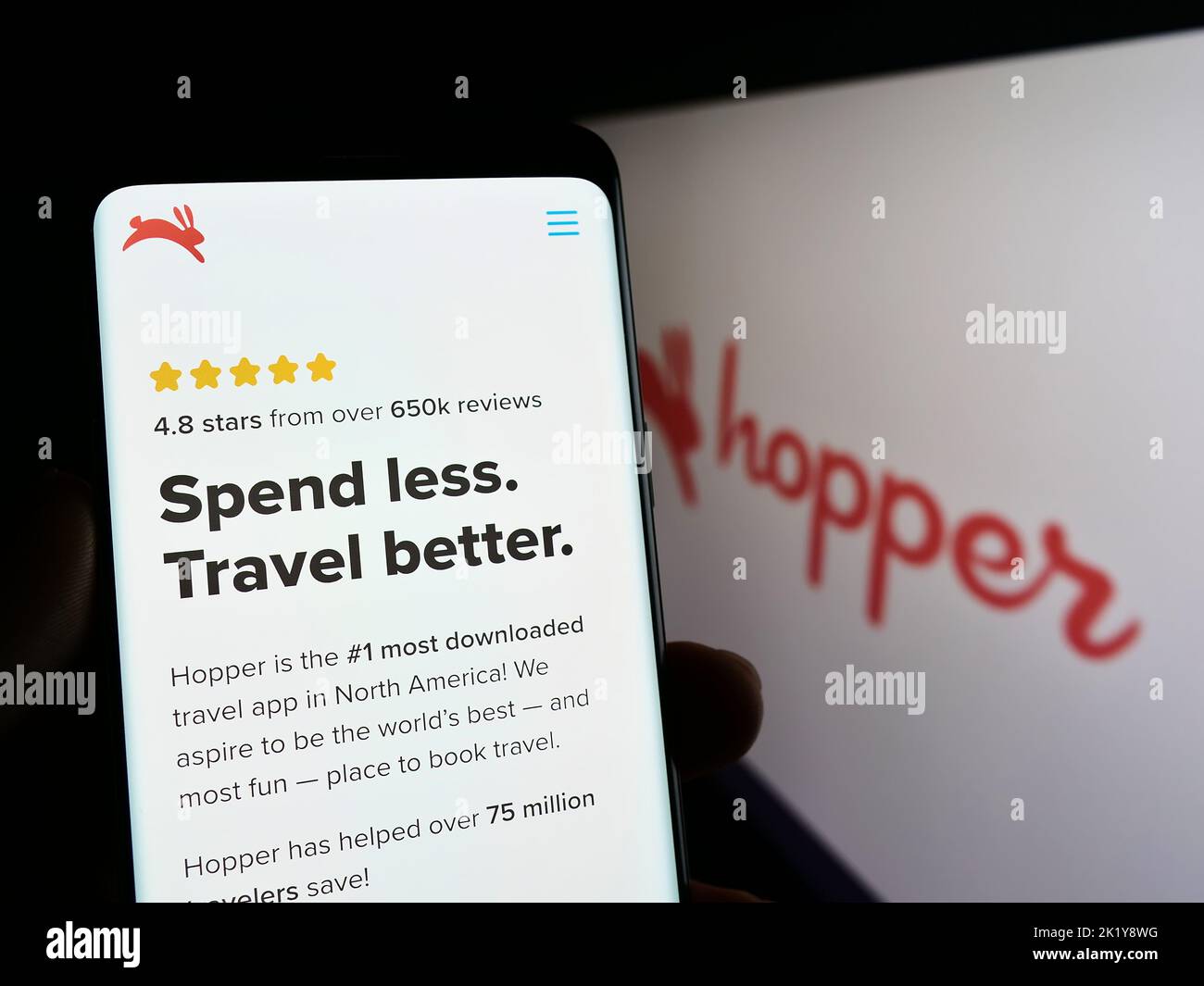 Person holding mobile phone with webpage of Canadian travel company Hopper Inc. on screen in front of logo. Focus on center of phone display. Stock Photo